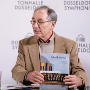 Georg Lauer stellt in der PK zum Jubiläum das Festbuch "MusikVereint" vor.