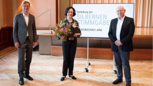 Verleihung der Silbernen Stimmgabel des Landesmusikrats 2021 an Marieddy Rossetto (Mitte) durch Holger Müller (links); die Laudatio hielt Rolf Kessler (rechts) ©vlago